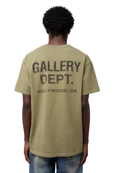 Back view of model wearing an olive green short sleeve T-shirt featuring oversized GALLERY DEPT. and Hollywood, CA typography printed across the upper back.