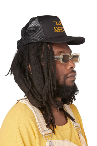 Left side profile of a model wearing the black trucker hat with a curved bill. The yellow front "GALLERY DEPT." logo is partially visible from the side, with black mesh panels extending around the back.
