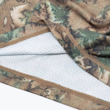 Close-up of the interior hem of a camouflage-print athletic T-shirt, showing the inner white perforated mesh panel, brown overlock stitching, and layered construction of the breathable fabric.