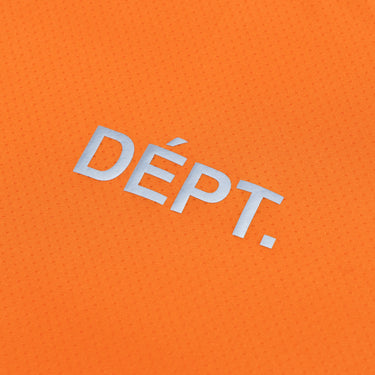 Close-up of the reflective silver “DÉPT.” logotype on the front of an orange long-sleeve athletic T-shirt, highlighting the lettering against the finely perforated fabric.