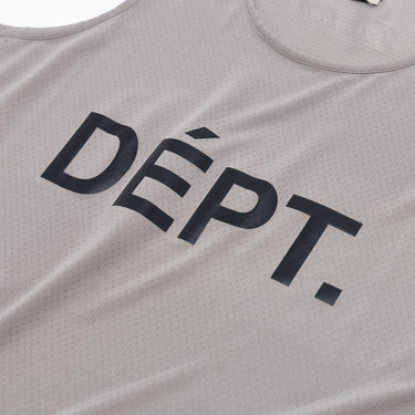Close-up of the dark “DÉPT.” logotype on the front of a taupe athletic tank top, highlighting the bold printed lettering and the fine perforated texture of the breathable fabric.