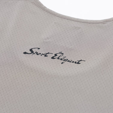 Close-up of the upper back of a taupe athletic tank top, showing the small dark “Sport Elegant” script lettering beneath the scoop neckline and the perforated fabric texture.