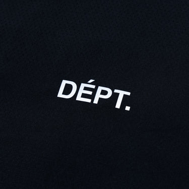 Close-up of the small white “DÉPT.” logotype on the front of a black athletic T-shirt, highlighting the printed lettering and the fine perforated texture of the fabric.