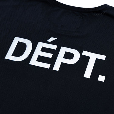 Close-up of the enlarged white “DÉPT.” logotype on the back of a black athletic T-shirt, highlighting the bold printed lettering against the black perforated fabric.
