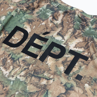 Close-up of the enlarged black “DÉPT.” logotype printed across the camouflage-patterned fabric on the back of an athletic T-shirt, highlighting the print and fabric texture. Displayed against a plain white background.