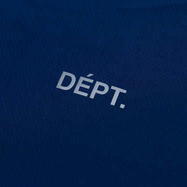 Close-up of the small white “DÉPT.” logotype on the front of a navy blue athletic T-shirt, highlighting the printed lettering and the fine perforated texture of the breathable fabric.