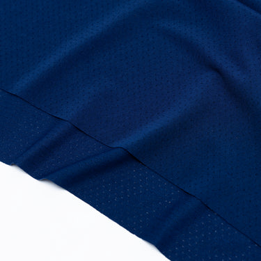 Close-up of the lower hem of a navy blue athletic T-shirt, showing the layered perforated fabric panel, tonal stitching, and textured breathable material. Displayed against a plain white background.