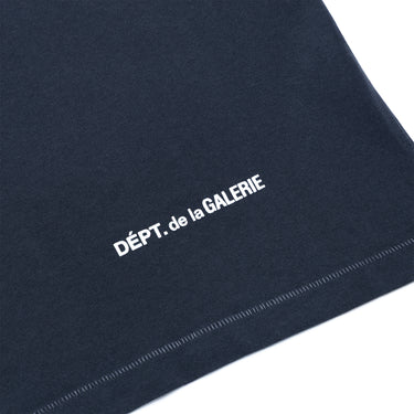 Close-up of dark gray fabric with a blue undertone, featuring white printed text reading “DÉPT. de la GALERIE” and a visible white stitched edge against a plain white background.