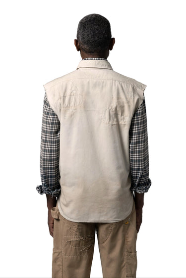 Back image of a male model in a cream-colored canvas utility vest over a black and white plaid shirt, paired with tan cargo pants on a white background.