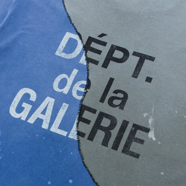 Angled close-up of the T-shirt, highlighting the enlarged “DÉPT. de la GALERIE” logotype printed across the contrasting blue and charcoal-gray panels, with curved black stitching dividing the fabrics and visible faded paint marks.