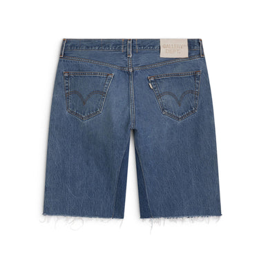 Back view of blue denim shorts laid flat against a white background, featuring two back pockets with curved contrast stitching, a light wash, and a white “GALLERY DEPT.” jacron on the upper right waistband. Contrasting denim panels run along the inner legs, and the hems are unfinished with loose frayed threads.