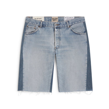 Front view of light-wash blue denim shorts laid flat against a white background, featuring a five-pocket design, darker blue contrasting panels along the outer legs, copper-tone stitching, belt loops, a button closure, and a zip fly. Multiple labels are visible along the waistband, and the raw hems are finished with loose frayed threads.